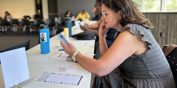Woman focused on her phone while sitting at a table with papers and water bottles.
