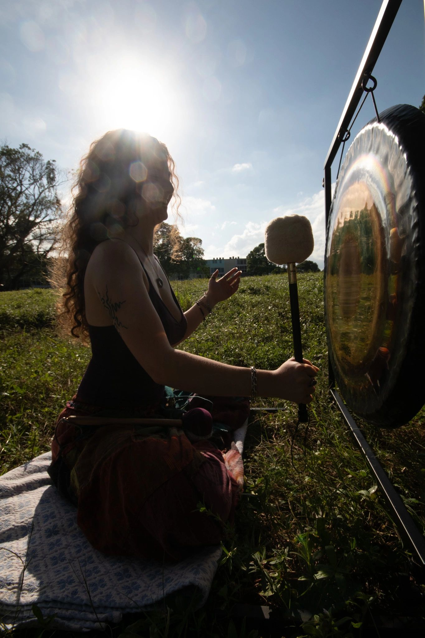 Person playing a gong outdoors with the sun shining behind them.