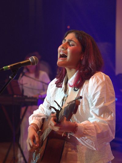 A woman passionately sings and plays guitar on stage.