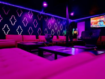 A vibrant lounge with purple lighting, modern furniture, and a patterned wall.