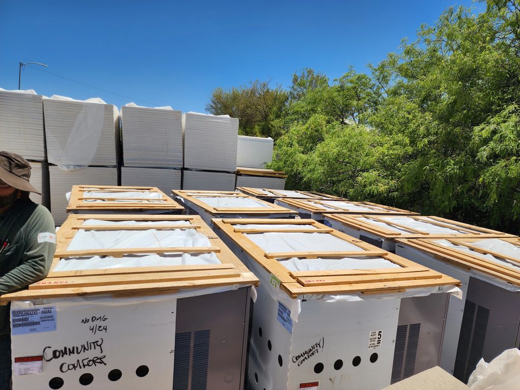 Stacked HVAC units wrapped and labeled for delivery under a clear blue sky.