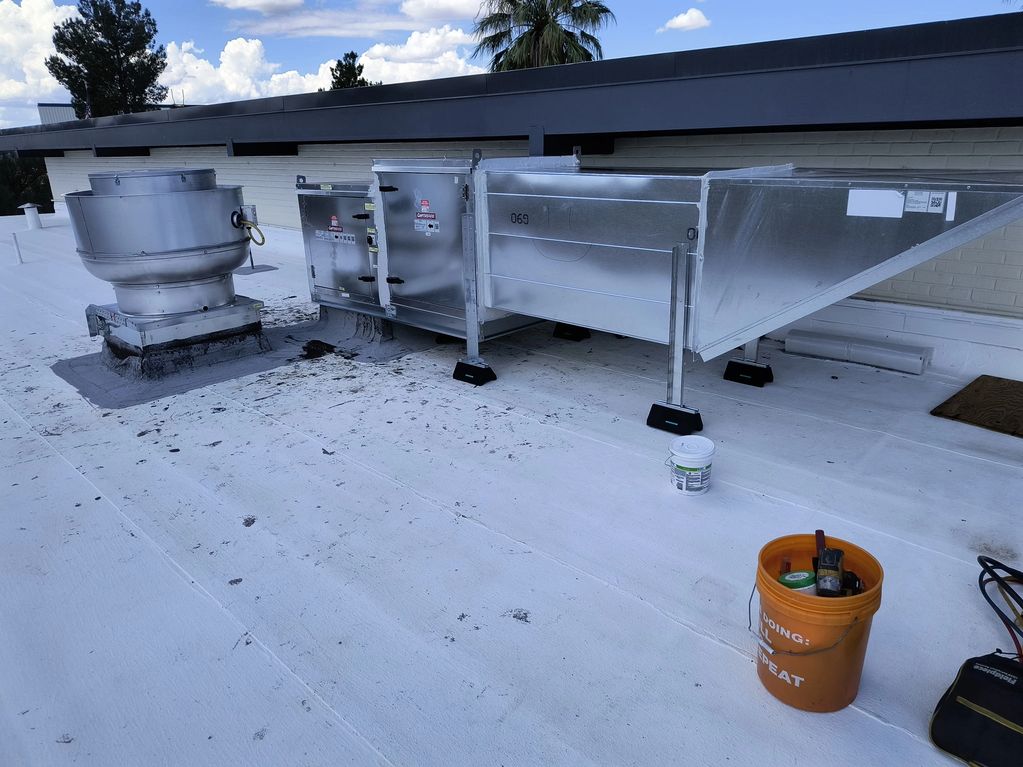 Rooftop HVAC system with ductwork and tools on a white roof under a blue sky.