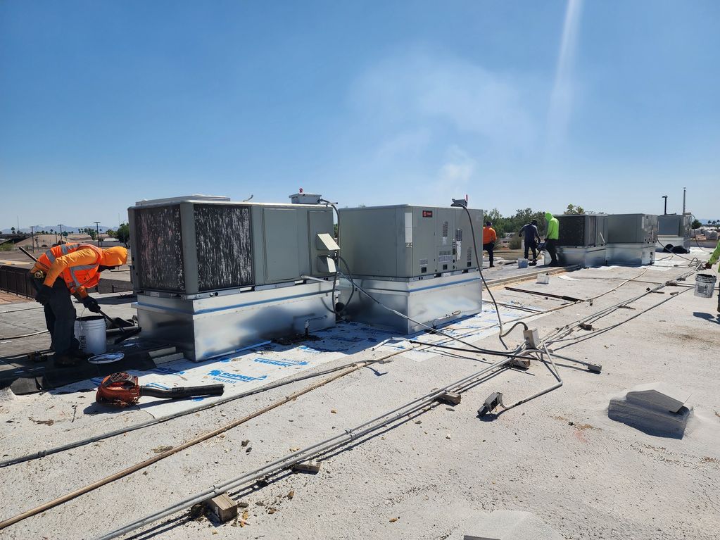 Workers in safety gear perform maintenance on rooftop HVAC units under a clear blue sky.