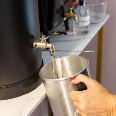 Hand filling a metal cup with water from a black dispenser tap.