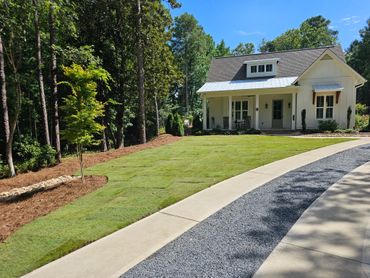 Charming white cottage with a manicured lawn and curved driveway on a sunny day.