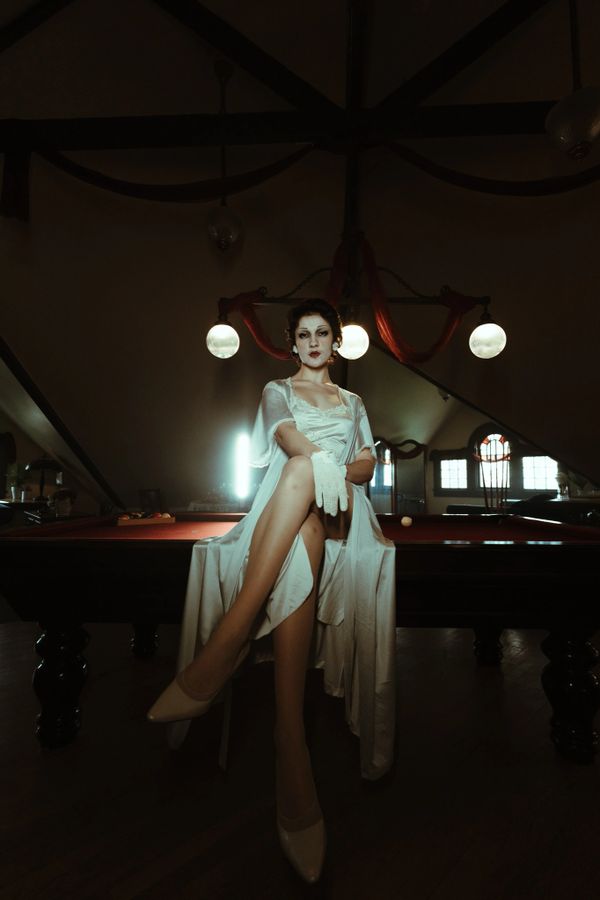 Woman in vintage attire sitting on a pool table under warm lighting.