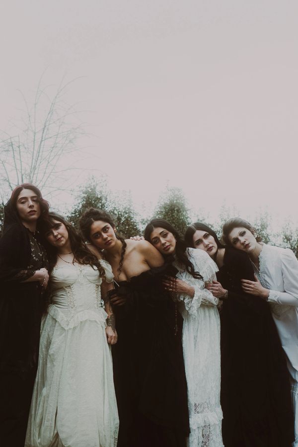 Six women in vintage black and white dresses closely standing outdoors under a gray sky.