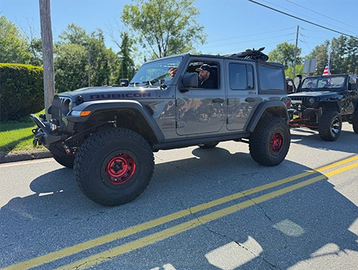 Gray Jeep Rubicon with red-rimmed tires parked on a sunny street.