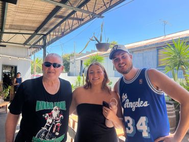 One participant and two support workers smiling outside under a sheltered area with plants, reflecti