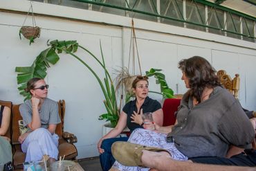 Three women engaged in a lively conversation in a cozy indoor setting with plants.