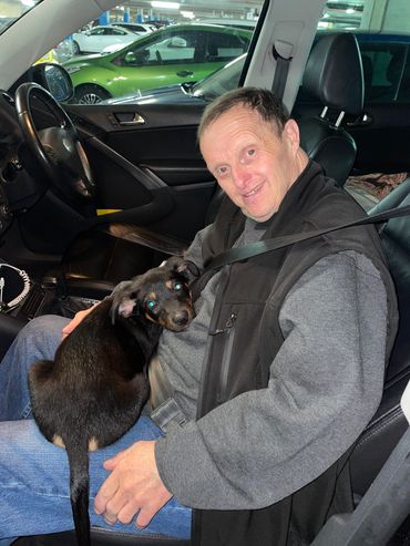 NDIS support and disability care in action as a participant sits happily in a car with a dog in Adel
