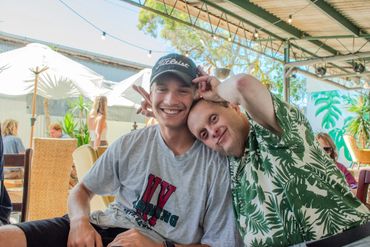 Two men smiling and posing playfully at an outdoor cafe.