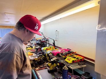 Man inspecting a remote control car on a workbench with several RC cars.