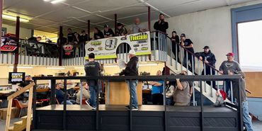 Group of people gathered on a platform and balcony indoors, watching or participating in an event.