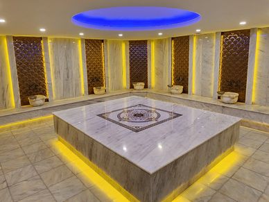 Luxurious marble steam room with blue ceiling light and yellow accent lighting.