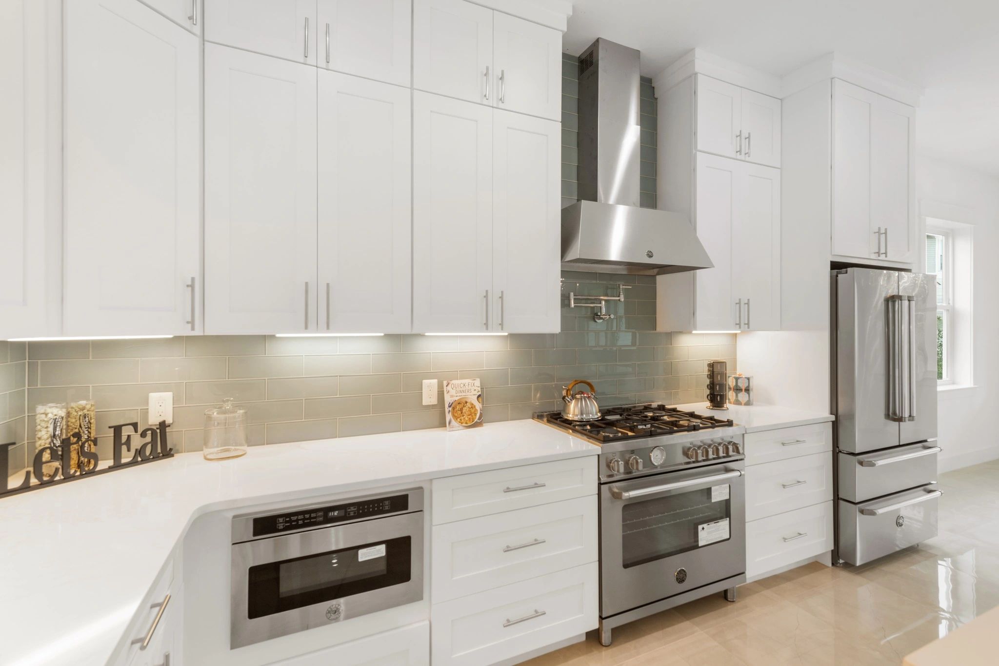 White kitchen cabinets and countertop, silver range and hood.