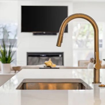 White countertops and view of sink from the side with focus on the gold faucet.