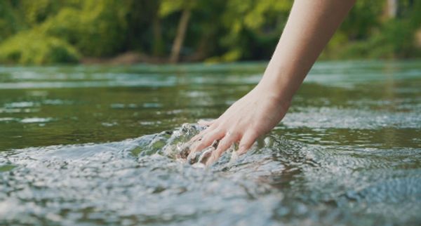 A hand gently touching the surface of a flowing river.