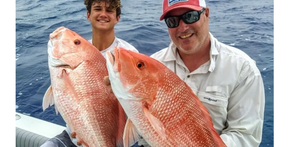 Two men proudly holding large red snapper fish on a boat in the ocean.