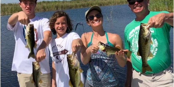 Four people proudly holding caught fish on a boat under a sunny sky.