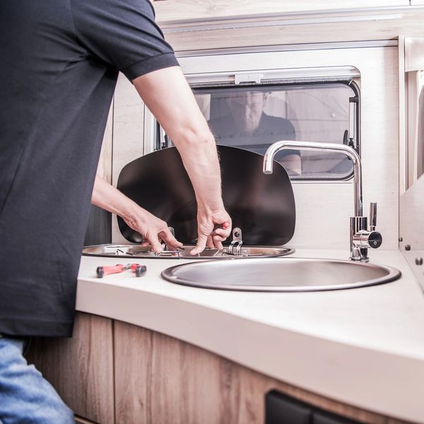 A man repairing a sink inside a caravan/motorhome