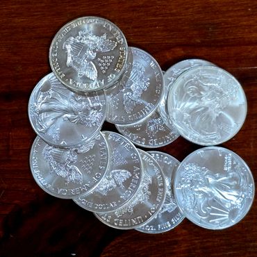 A pile of shiny American silver dollar coins on a wooden surface.