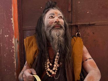 A man with face paint and traditional attire holding a brass vessel.