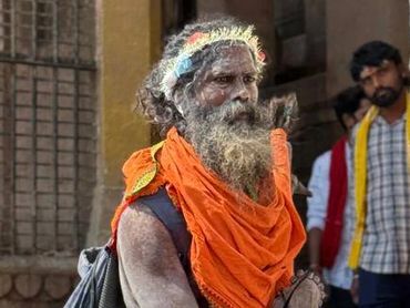 A holy man in bright orange attire playing a small drum on a street.