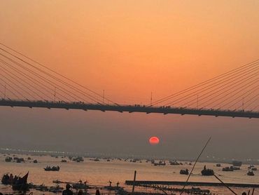 Sunset over a river with boats and a modern bridge.