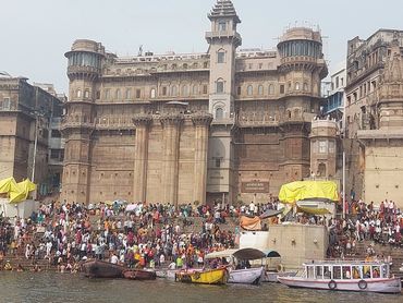 Crowds gather at Darbhanga Ghat by the river with historic architecture in the background.