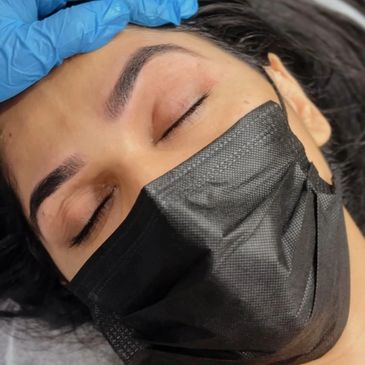 Person with freshly shaped eyebrows wearing a black mask and blue gloves.