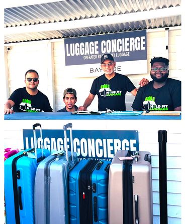 Four luggage concierge workers stand behind a counter with several suitcases in front.