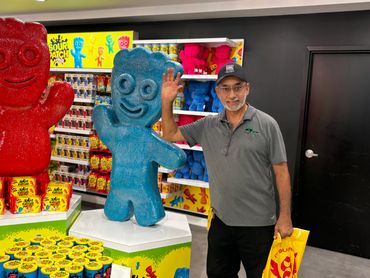 Man posing with large colorful Sour Patch Kids statues in a candy store.