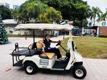 A woman sits in a luggage concierge golf cart outdoors.