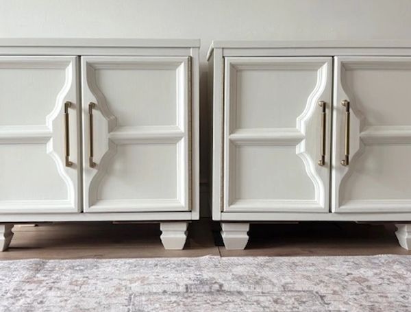 Two white cabinets with gold handles on a patterned rug.