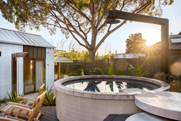 Outdoor hot tub and wooden chairs with sunlight through trees.