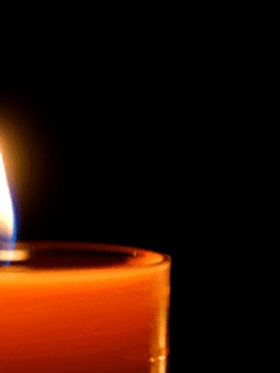 A single lit orange candle glowing against a black background.
