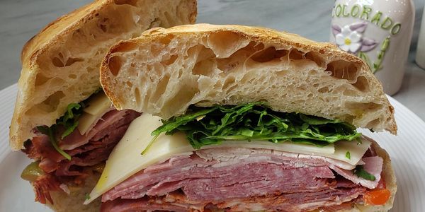 A deli sandwich with meat, cheese, and lettuce on ciabatta.