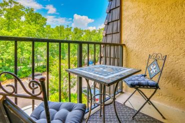 Cozy balcony with mosaic table and cushioned chairs overlooking green trees off second bedroom.