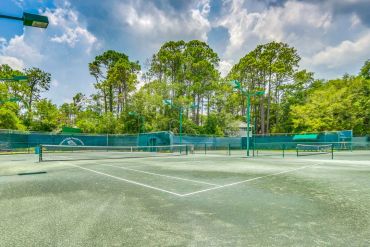 Resort outdoor tennis court surrounded by trees and fencing.