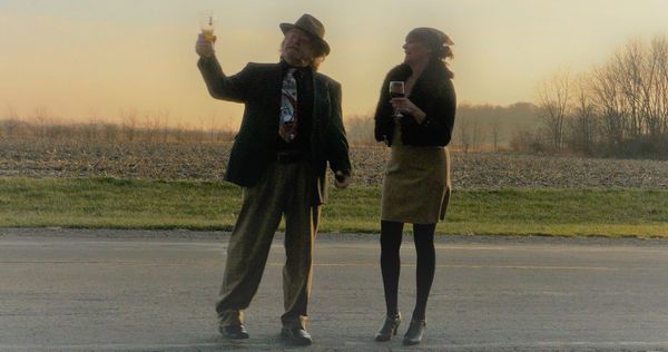 Two people standing on a road at sunset, holding drinks.