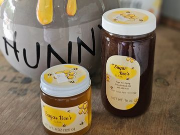 Two jars of Sugar Bee's honey in front of a pot labeled HUNNI.