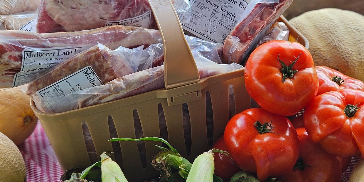 Basket of packaged meats with fresh tomatoes, corn, and melons.
