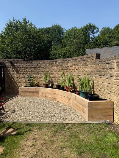 Curved wooden planter with potted plants against a brick wall.