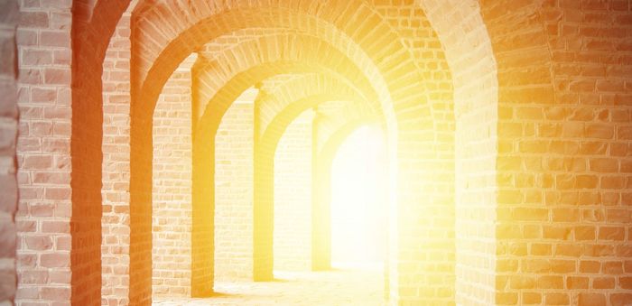 Sunlight floods through a series of brick arches creating a warm, glowing corridor.