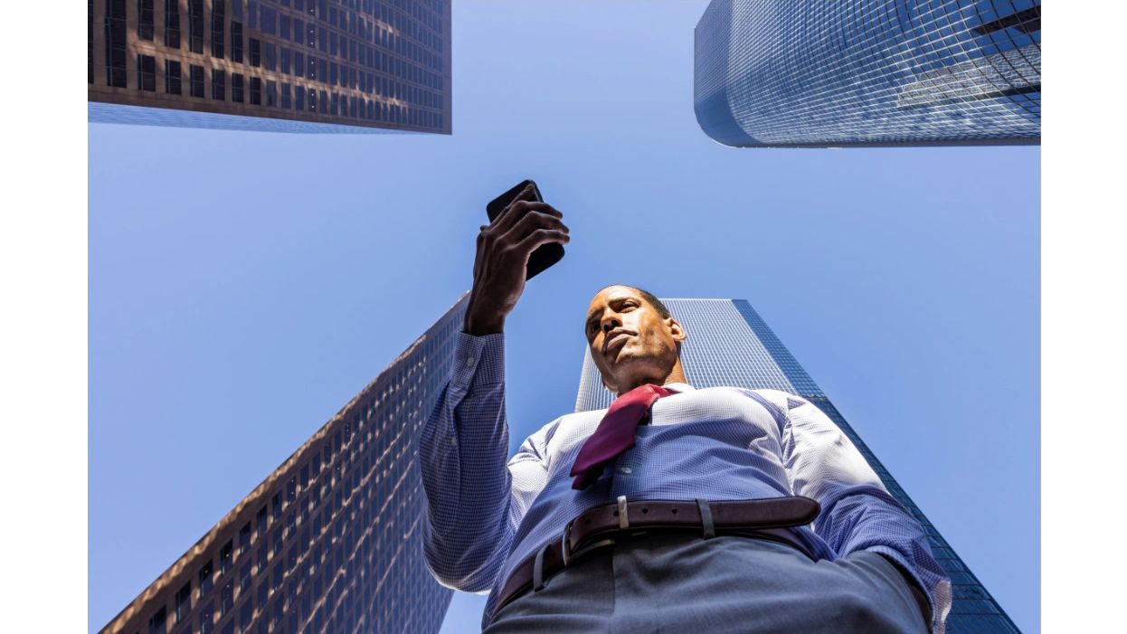 Photo of man reading his cell phone among skyscrapers. The photo is next to how to contact NMS.