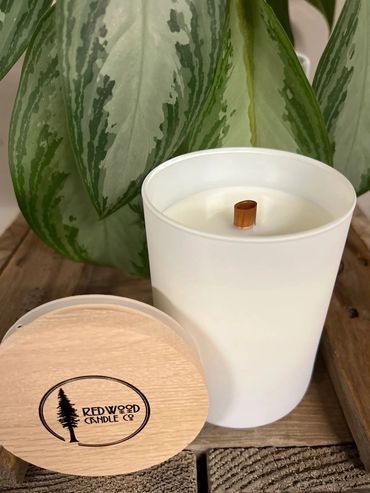 Coconut and beeswax candles in a matte white glass container with a wooden wick and a wooden lid.
