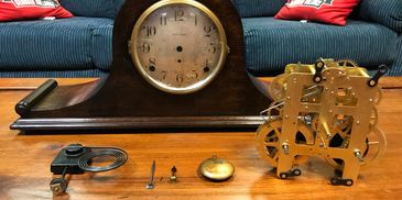 Disassembled antique mantel clock parts on a wooden table.