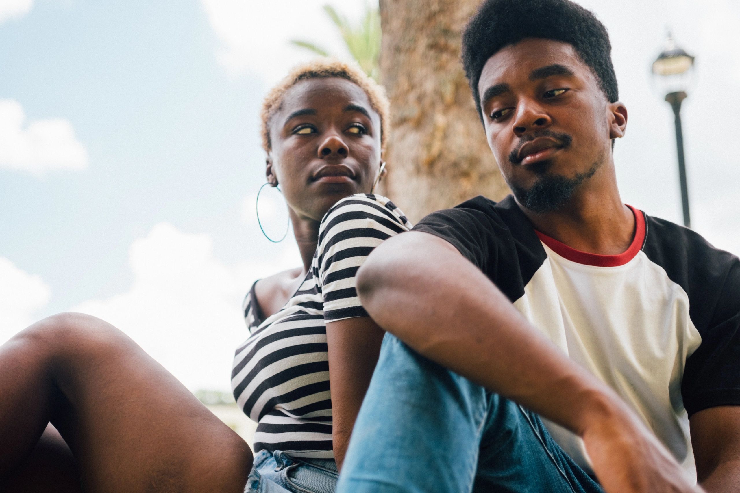 Two young adults sitting outdoors, looking at each other.