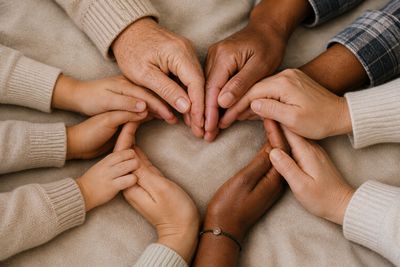 Multiple hands forming a heart shape together on a beige surface.